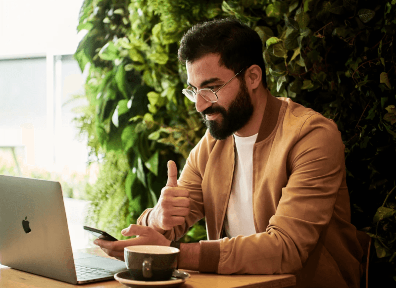 man giving a thumbs-up while on his phone and computer